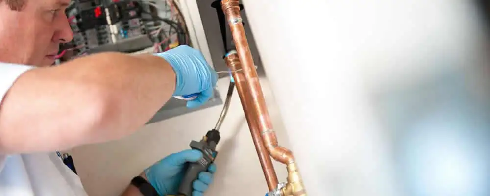 Water heater repair technician testing copper pipe connections and controls in Tacoma, WA